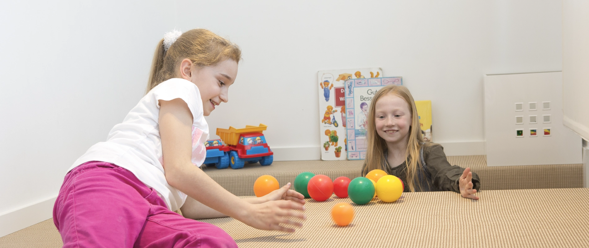 Aufnahme von zwei jungen Mädchen im Wartebereich beim Spielen mit kleinen Bällen.